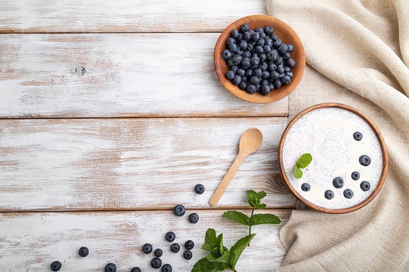 Yogurt with blueberry in wooden bowl on white wooden background and linen textile. top view, flat lay, copy space