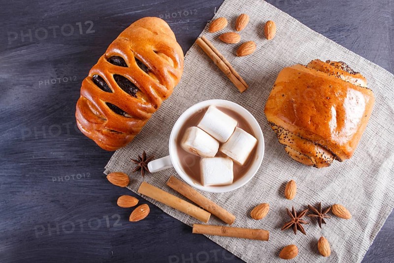 A cup of hot chocolate with marshmallow, buns and spices on linen napkin and black wooden background. top view, copy space