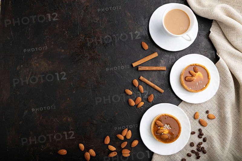Sweet tartlets with almonds and caramel cream with cup of coffee on a black concrete background and linen textile. top view, flat lay, copy space