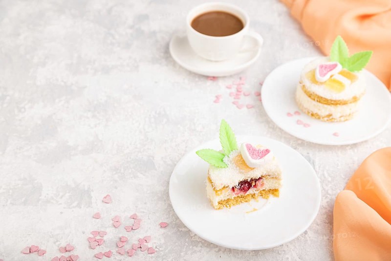 Decorated cake with milk and coconut cream with cup of coffee on a gray concrete background and orange textile. Side view, copy space