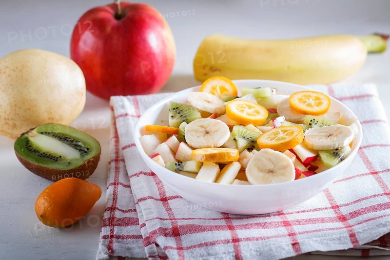 Vegetarian salad of bananas, apples, pears, kumquats and kiwi on linen tablecloth, close up, selective focus. white wooden background