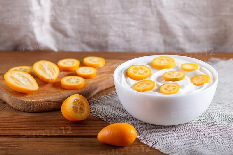 Greek yogurt with kumquat pieces in a white plate on a brown wooden background, close up