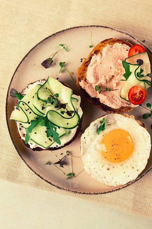 Assortment of sandwiches, white bread, fried egg, cream cheese and cucumber, capelin caviar, sesame bun, breakfast, on a white table, no people
