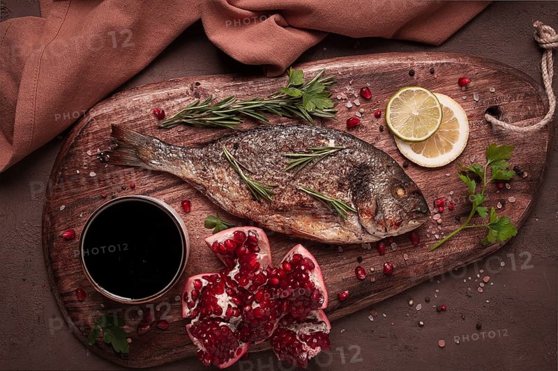 Fried dorado fish, with spices and herbs, on a wooden board, pomegranate sauce, close-up, no people