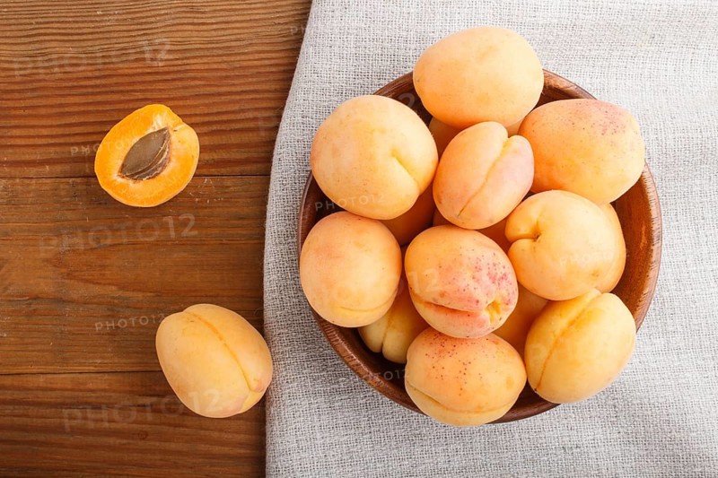 Fresh orange apricots in wooden bowl on wooden background. top view, flat lay, close up