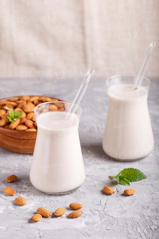 Organic non dairy almond milk in glass and wooden plate with almond nuts on a gray concrete background. Vegan healthy food concept, close up, side view