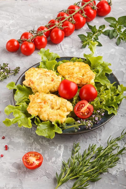 Minced chicken cutlets with lettuce, tomatoes and herbs on a gray concrete background. side view, close up