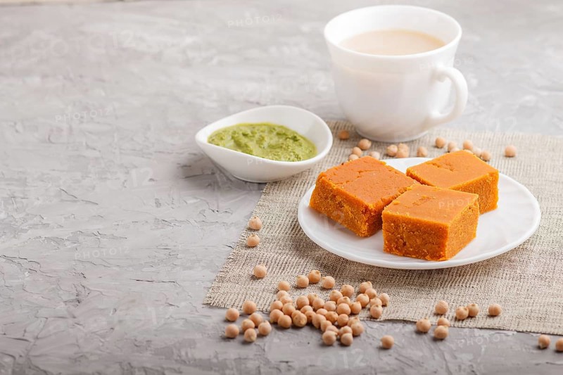 Traditional indian candy burfi in white plate with mint chutney on a gray concrete background. side view, copy space