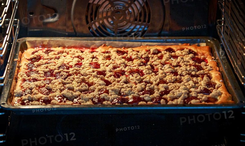 A plum tart with red plums and crumb topping is baking in the oven, ready for perfection