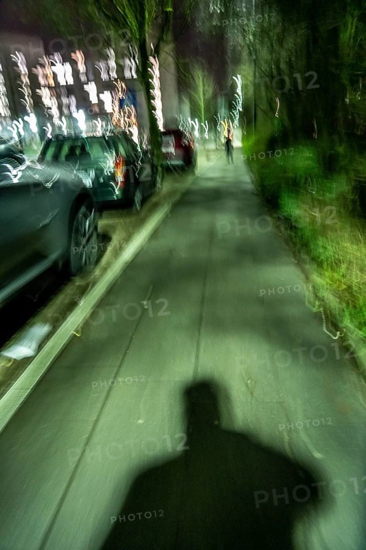 Pedestrian path in the evening, dark, little lighting from street lamps, shadow of a man, following another person