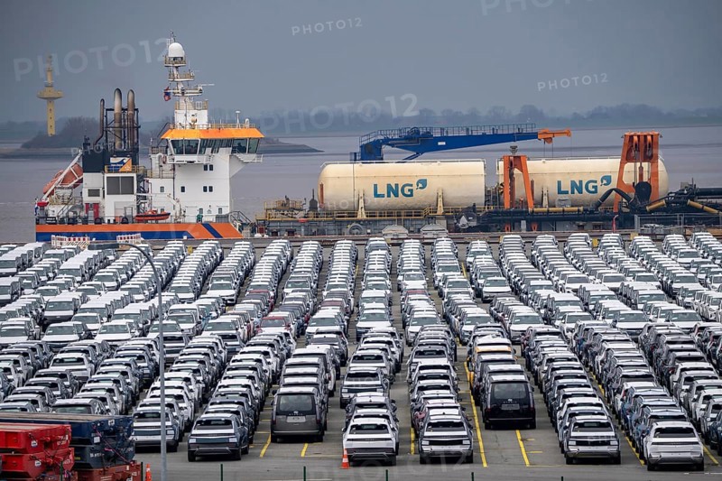 Parking space for import vehicles, hundreds of Hyundai Ioniq, electric cars, waiting for onward transport, behind them, on the Weser, the dredger, the hopper dredger, suction dredger, Vox Ariane, which holds the tug to a certain depth, at the EUROGATE container terminal in the overseas port of Bremerhaven, Lower Saxony, Germany, Europe