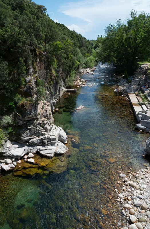 Klarer Fluss, der durch eine felsige, bewaldete Landschaft fließt, mit grünem Ufer und blauem Himmel, Römische Brücke, Piscina natural de Madrigal de la Vera, Naturbad Madrigal de la Vera, Garganta de Alardos, Schlucht Alardos, Cáceres, Extremadura, Spanien