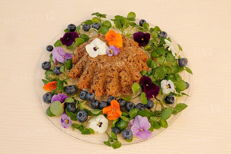 Vegetarian cuisine, chestnut roast, chestnut cake, chestnut roast, chestnut cake with hazelnuts, chestnut cake, savoury, vegan, salty, baked, from the oven, healthy, main course, glass plate, new cuisine, decoration with pansies, violet (Viola), blueberries (Vaccinium), blueberries, food photography, studio, Germany, Europe