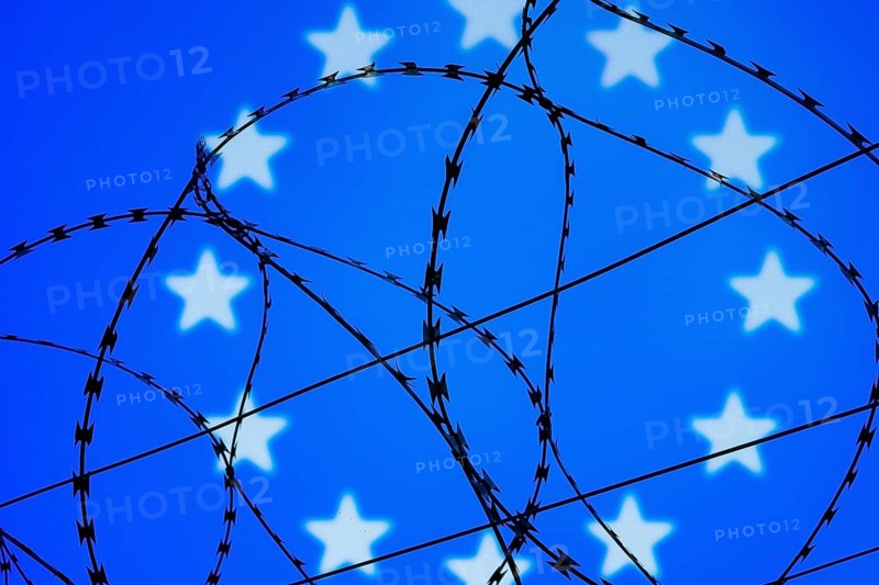 Symbolic image, migration, defence against refugees wanting to enter the EU, barbed wire overarches the stars of the EU flag against a blue sky, border, border fence