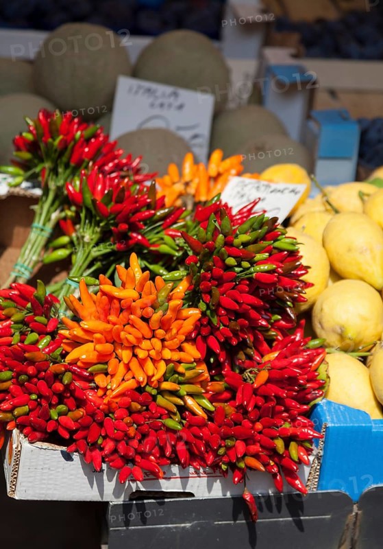 Different coloured peppers on a market stall next to other fruits