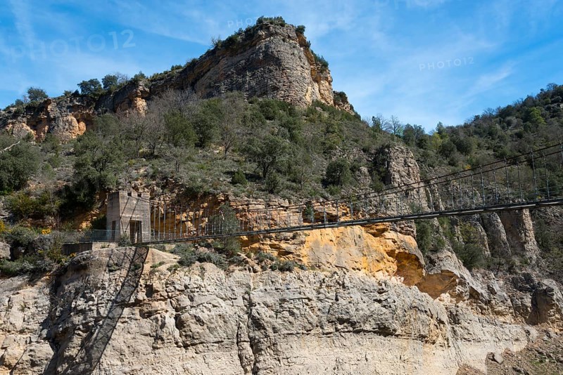 A rocky mountain landscape with dense vegetation under a bright blue sky, suspension bridge, Noguera Ribagorçana Mont-rebei Natural Park, Montsec mountain range, Noguera Ribagorçana river, Lleida province, Catalonia, Aragon, Spain, Europe