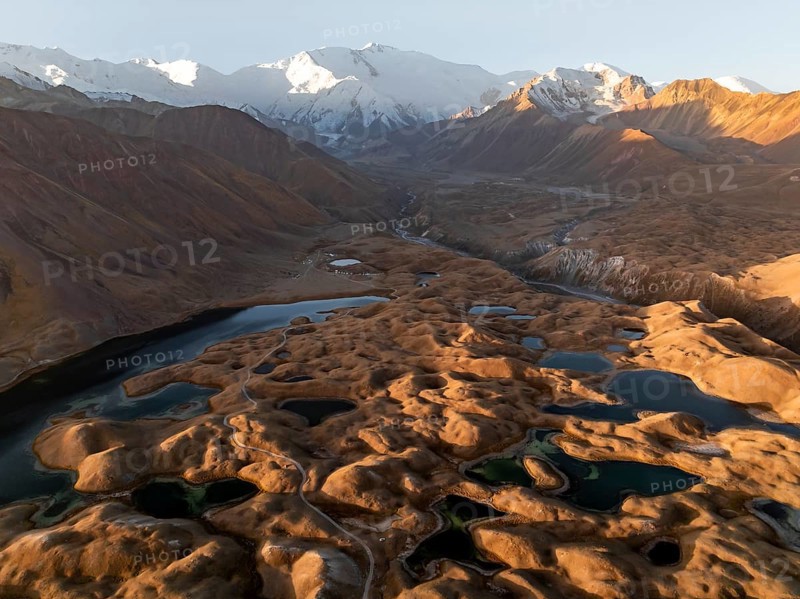 White glaciated and snowy mountain peak Pik Lenin at sunrise, hilly landscape with golden yellow meadows and lakes, aerial view, Trans Alay Mountains, Pamir Mountains, Osher Province, Kyrgyzstan, Asia