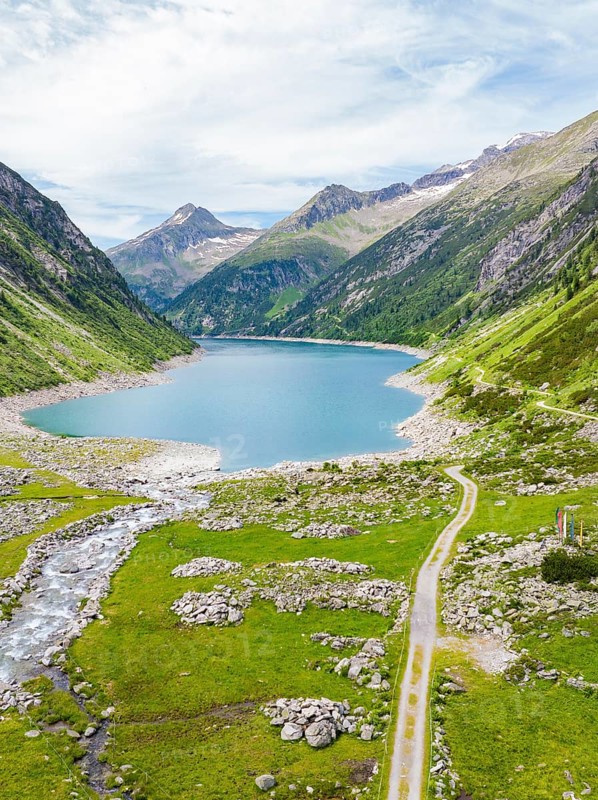 A mountain lake surrounded by green meadows and mountains, with a river and a hiking trail, under a slightly cloudy sky, Klein Tibet, Zillertal, Austria, Europe