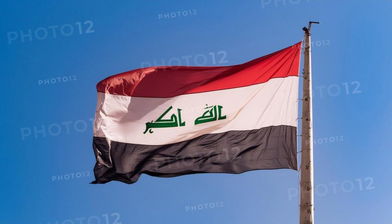 The flag of Iraq flutters in the wind, isolated against a blue sky