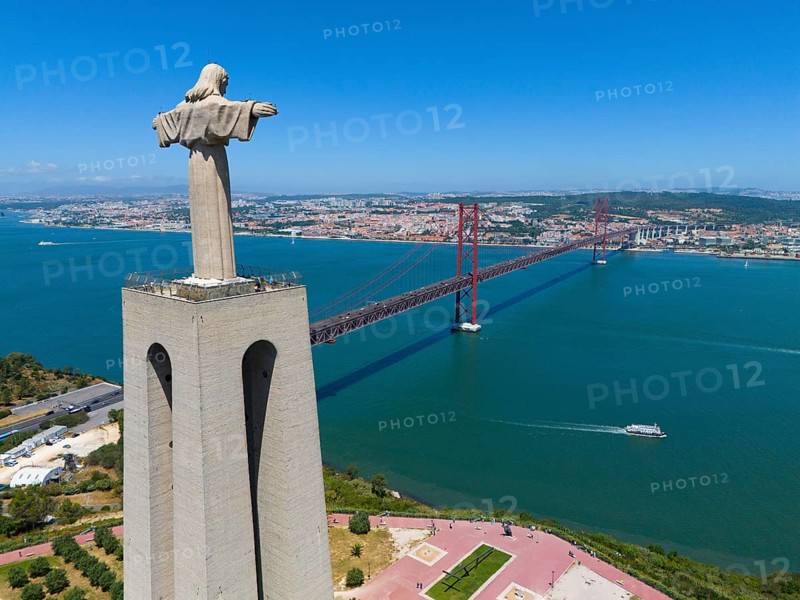 Statue with outstretched arms on a viewpoint next to a red bridge and an extensive cityscape in the background, aerial view, Statue Cristo Rei, Almada, Ponte 25 de Abril, 25 April Bridge, suspension bridge over the Tagus, double-decker bridge, road traffic and railway traffic, Lisbon, Lisboa, Portugal, Europe