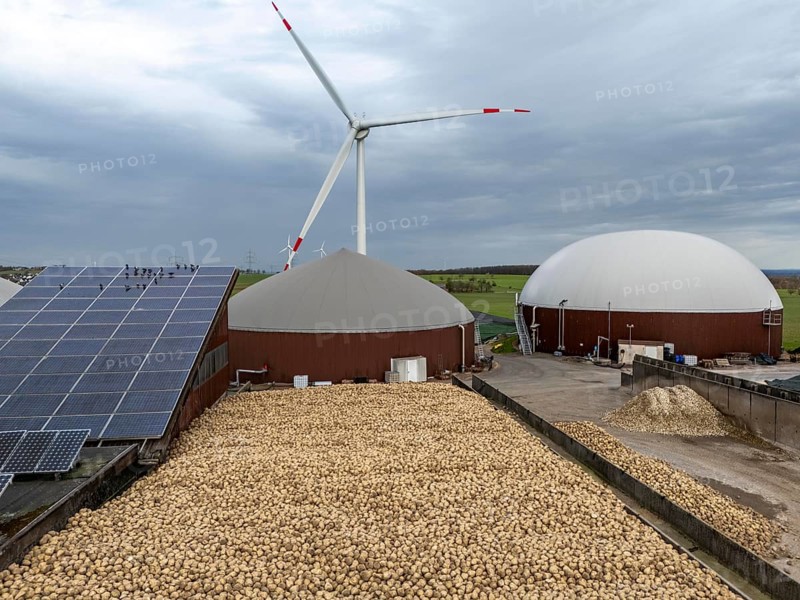 Biogas plant produces gas from various biomass, here the sugar beet store, the electricity is produced in combined heat and power plants with the biogas produced and sold to companies in the neighbouring industrial estate, the heat generated is fed into a local heating network, gas storage technical building with solar roofs and wind power plant, Ense, North Rhine-Westphalia, Germany, Europe