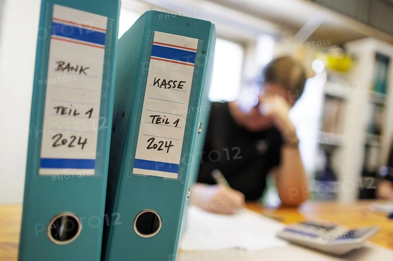 Symbolic photo: A woman sits at a desk in an office with a calculator and file folders and does bookkeeping. Berlin, 14.08.2024