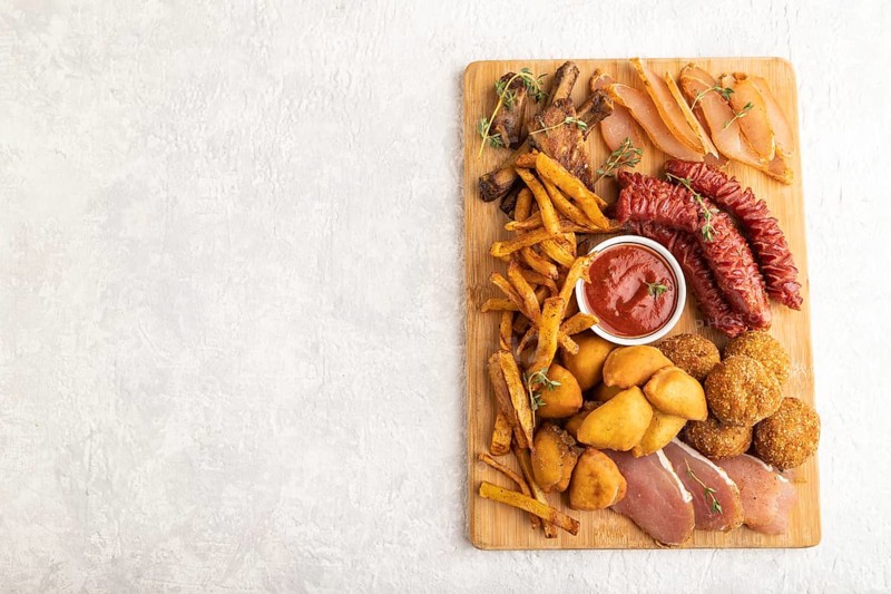 Set of snacks: sausages, fried potatoes, meat balls, dumplings, basturma on a cutting board on a gray concrete background. Top view, flat lay, close up, copy space