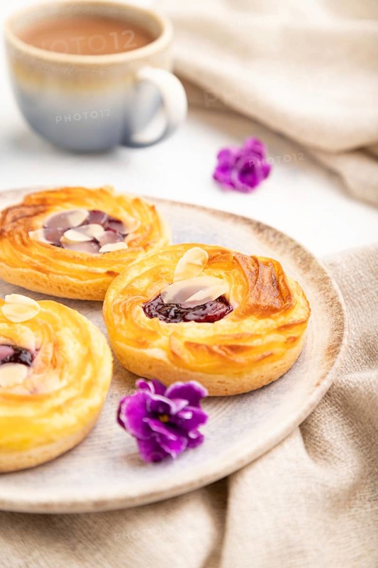 Small cheesecakes with jam and almonds with cup of coffee on a white concrete background and linen textile. Side view, close up, selective focus