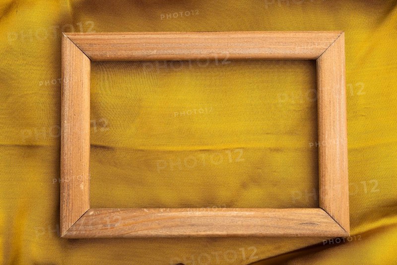 Wooden frame on smooth yellow silk tissue. Top view, flat lay, natural textile background and texture