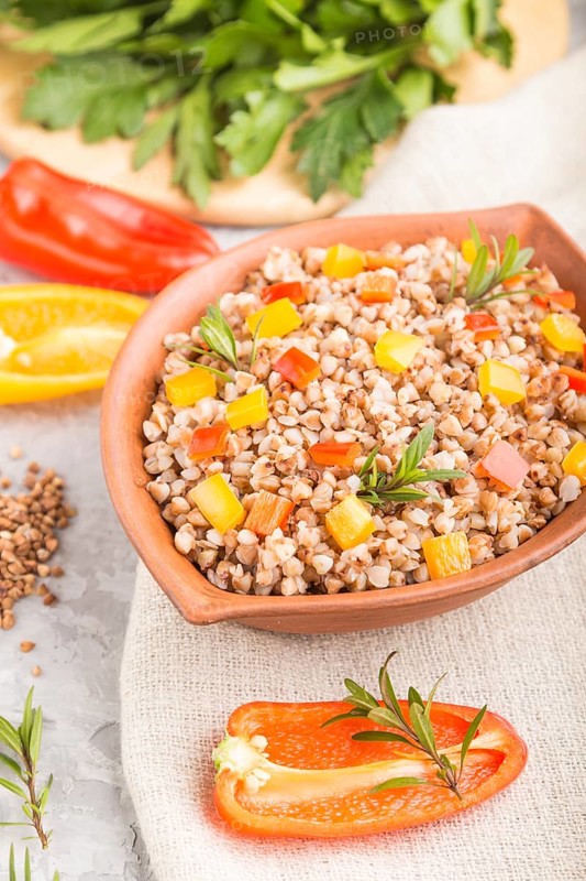 Buckwheat porridge with vegetables in clay bowl on a gray concrete background and linen textile. Side view, selective focus, close up. Russian traditional cuisine