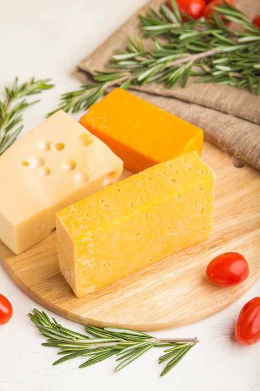 Various types of cheese with rosemary and tomatoes on wooden board on a white wooden background and linen textile. Side view, close up, close up, selective focus