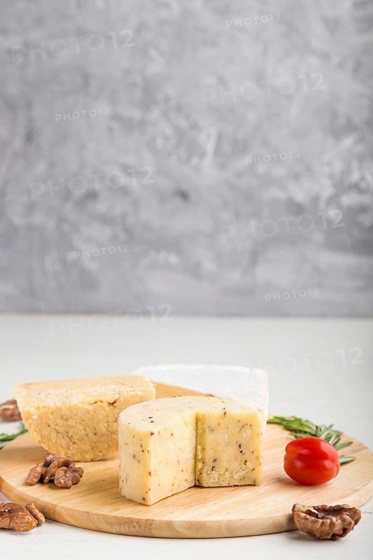 Cheddar and various types of cheese with rosemary and tomatoes on wooden board on a gray and white background. Side view, copy space, selective focus