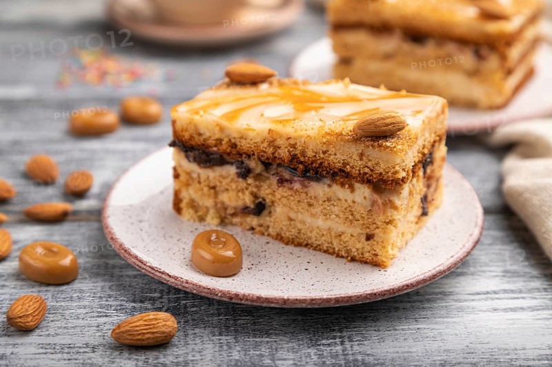 Honey cake with milk cream, caramel, almonds and a cup of coffee on a gray wooden background and linen textile. Side view, close up, selective focus