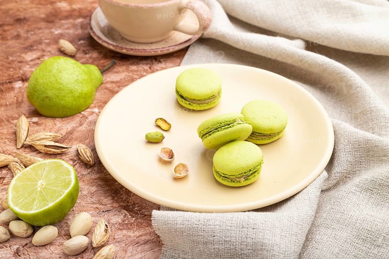 Green macarons or macaroons cakes with cup of coffee on a brown concrete background and linen textile. Side view, close up
