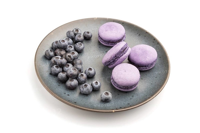 Purple macarons or macaroons cakes with blueberries on ceramic plate isolated on white background. Side view, close up