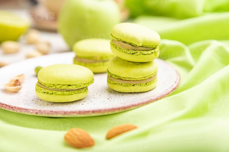 Green macarons or macaroons cakes with cup of coffee on a white wooden background and green linen textile. Side view, close up, selective focus