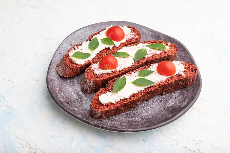 Red beet bread sandwiches with cream cheese and tomatoes on white concrete background. Side view, close up