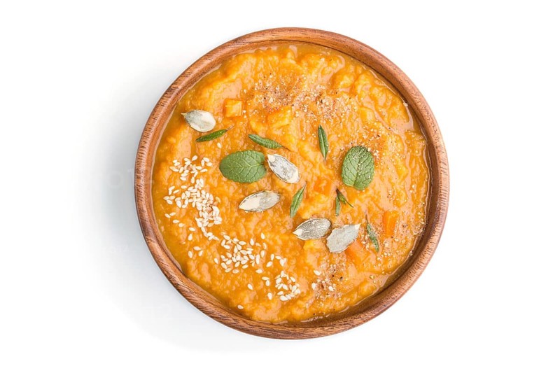Sweet potato or batata cream soup with sesame seeds in a wooden bowl isolated on a white background. top view, close up