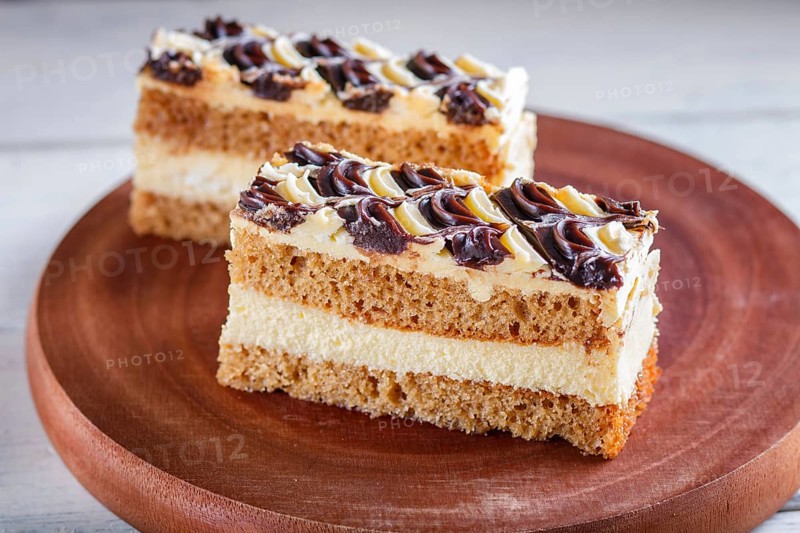 A piece of cake with milk and butter cream on a wooden kitchen board, close up, selective focus, white background