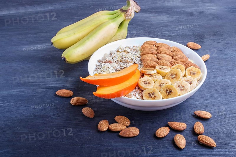 A plate with muesli, almonds, banana, sliced persimmon on a black wooden background. close up. copy space