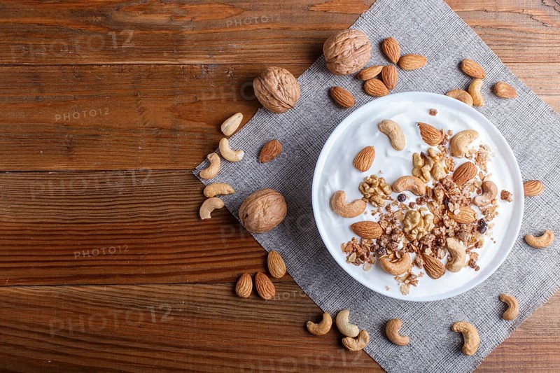 White plate with greek yogurt, granola, almond, cashew, walnuts on brown wooden background. top view. copy space