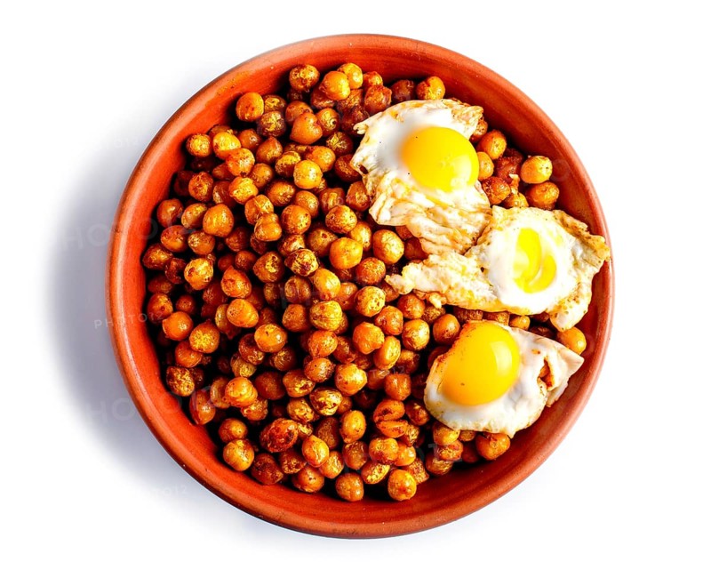 Fried chickpeas with quail eggs and spices in a clay plate isolated on white background, top view