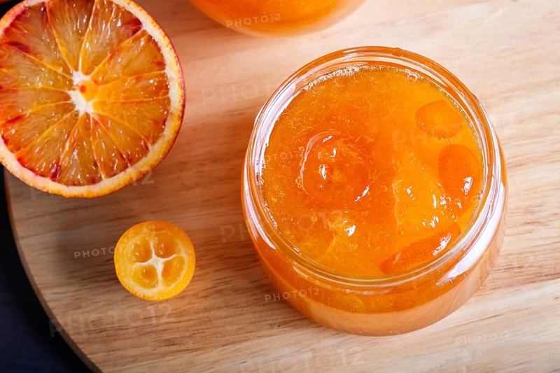 Orange and kumquat jam in a glass jar with fresh fruits on a wooden kitchen board. Homemade, close up, top view