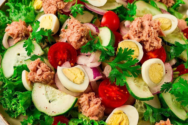 Tuna salad, vegetable salad with quail eggs, lettuce, red onion and cucumbers, on a light gray table, keto food, lifestyle, healthy eating, selective focus, top view, no people