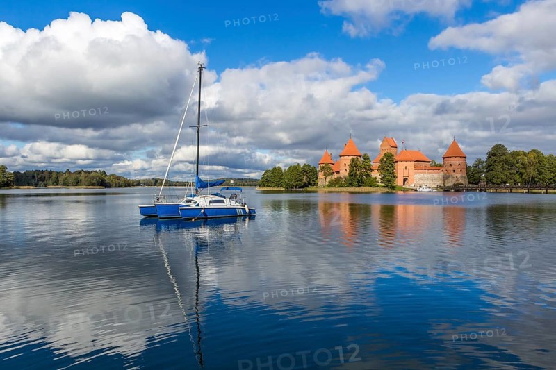 Blue yacht on Galve lake, Lithuania with Trakai castle and cloudy sky on background