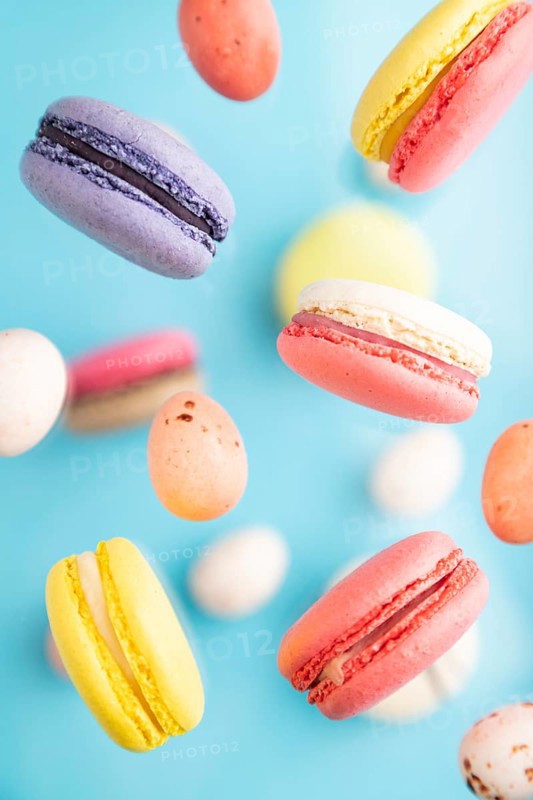 Multicolored flying macaroons and chocolate eggs frozen in the air on blurred blue background. top view, flat lay, close up. Breakfast, morning, concept