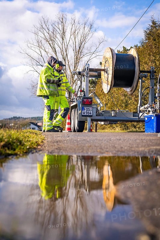 Worker inspecting a cable drum next to a reflective pool of water, fibre optic construction, Nagold, Black Forest, Germany, Europe