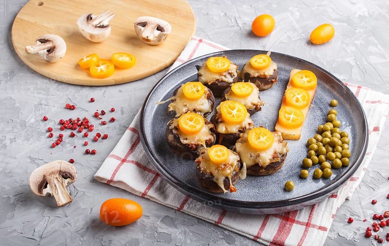 Stuffed fried champignons with cheese, kumquats and green peas on a gray concrete background. ceramic plate, side view, close up, horizontal