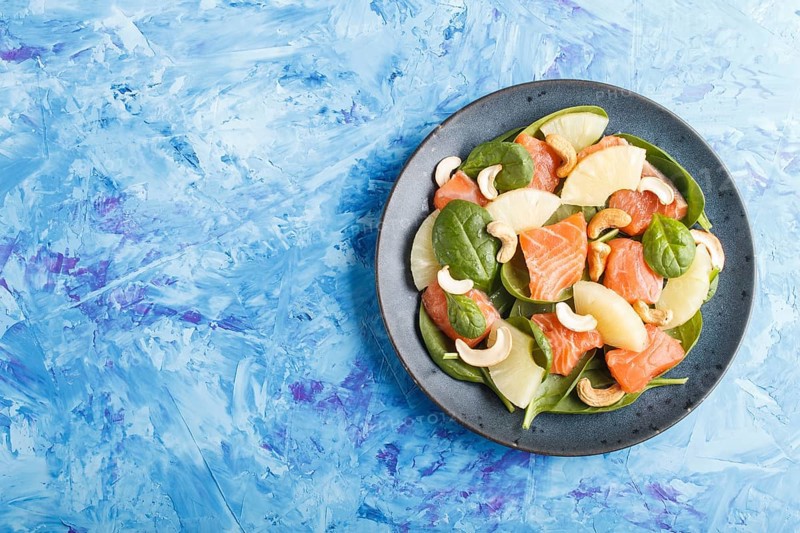 Fresh salmon with pineapple, spinach and cashew on a blue concrete background. Top view, copy space, flat lay