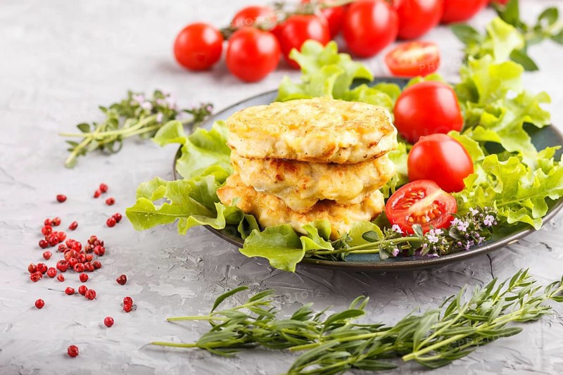 Minced chicken cutlets with lettuce, tomatoes and herbs on a gray concrete background. side view, close up, selective focus